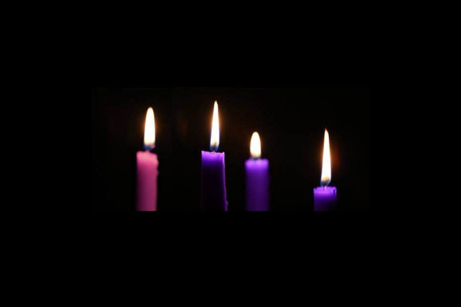 Three purple and one pink candle alight on a black background