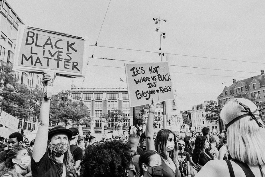 A black and white photo of a Black Lives Matter protest. There are two signs, one reads, "Black Lives Matter" the other, "It is not white vs black, its everyone vs racists"