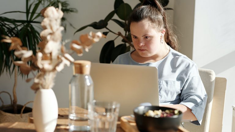 A women with down syndrome is reading something from her laptop in a modern apartment.