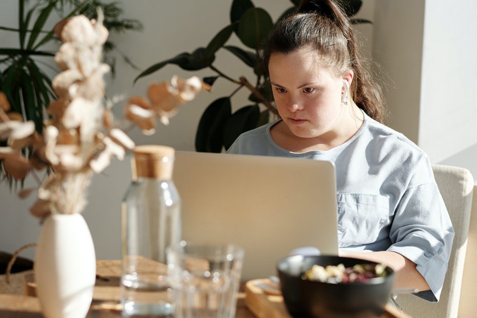A women with down syndrome is reading something from her laptop in a modern apartment.
