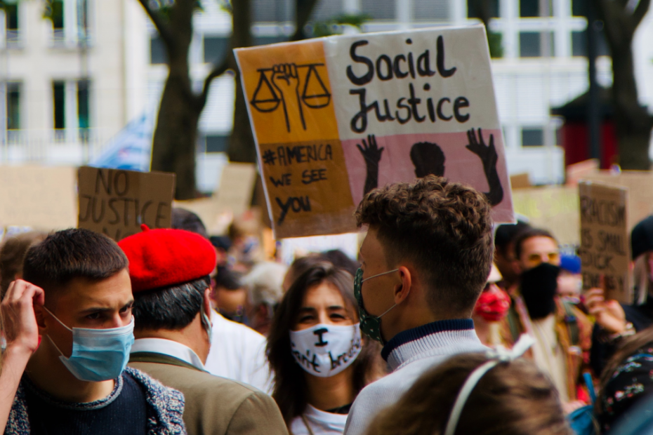A crowd of people marching, with a sign in the background reading "Social Justice"
